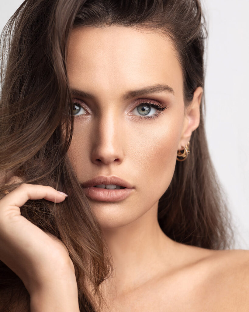 Final retouched glamour portrait with dramatic smoky eyes, glossy nude lips, and large gold pearl drop earrings, showcasing flawless skin texture