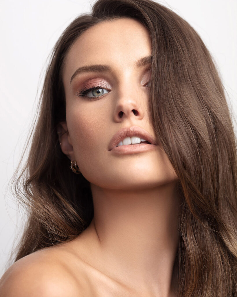 Flawless, high-end retouched beauty portrait emphasizing the model's eyes, natural-looking glossy lips, and perfectly smooth skin texture.