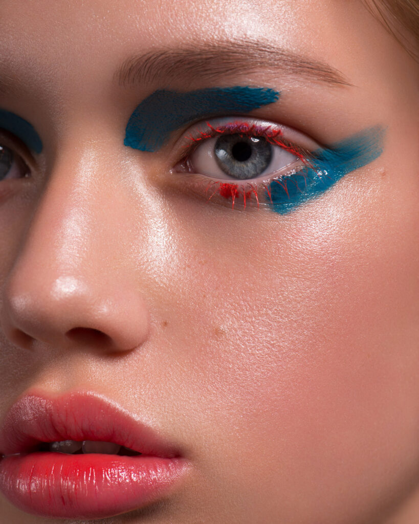 Macro close-up professional retouching of an artistic beauty look with graphic blue and red eyeliner, emphasizing glossy skin and vibrant color pop