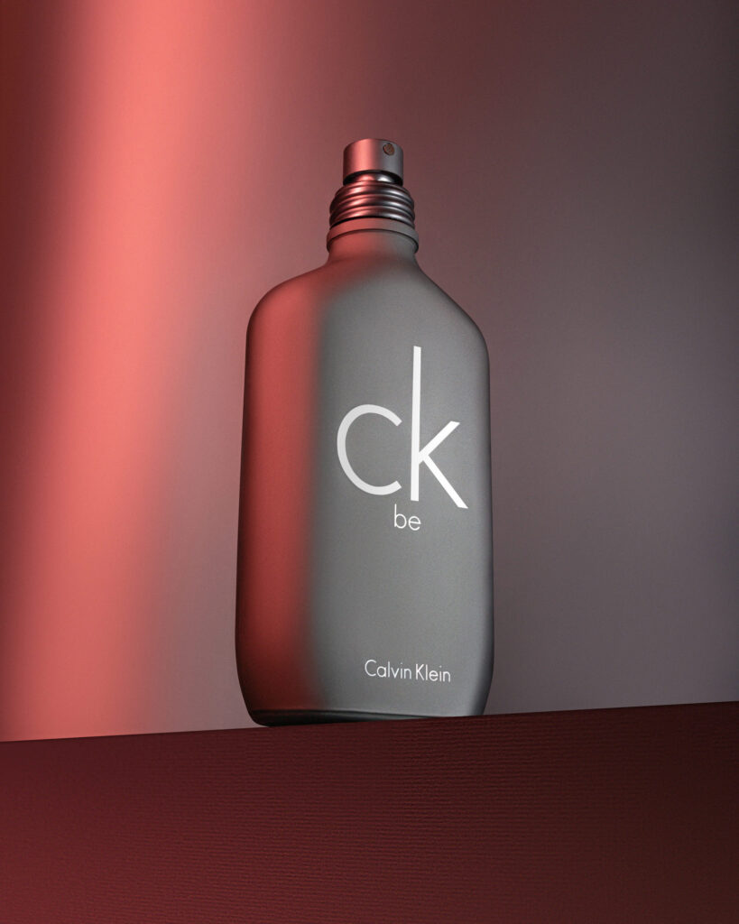 Calvin Klein CK Be matte grey perfume bottle shown close-up with dramatic, moody red and dark grey lighting, emphasizing a sensual, editorial style.