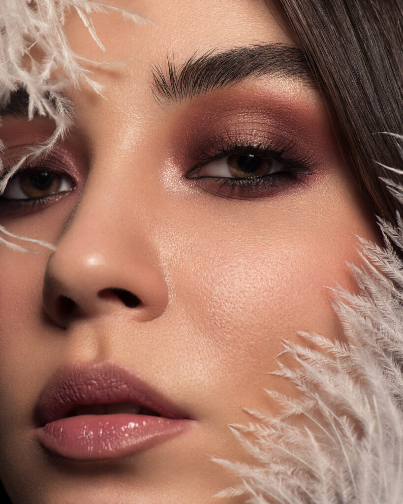 High-end retouched glamour portrait with dramatic eye makeup, glossy pink lips, and large rose gold statement earrings, showcasing flawless skin and perfect hair detail.