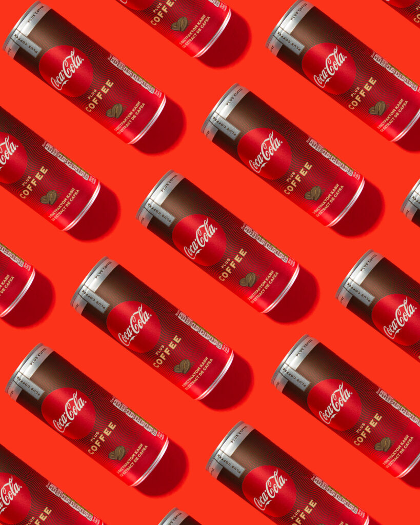 Seamless repeating pattern of red and brown Coca-Cola Plus Coffee cans, arranged diagonally on a vibrant red background, shot from a high angle for dynamic effect.