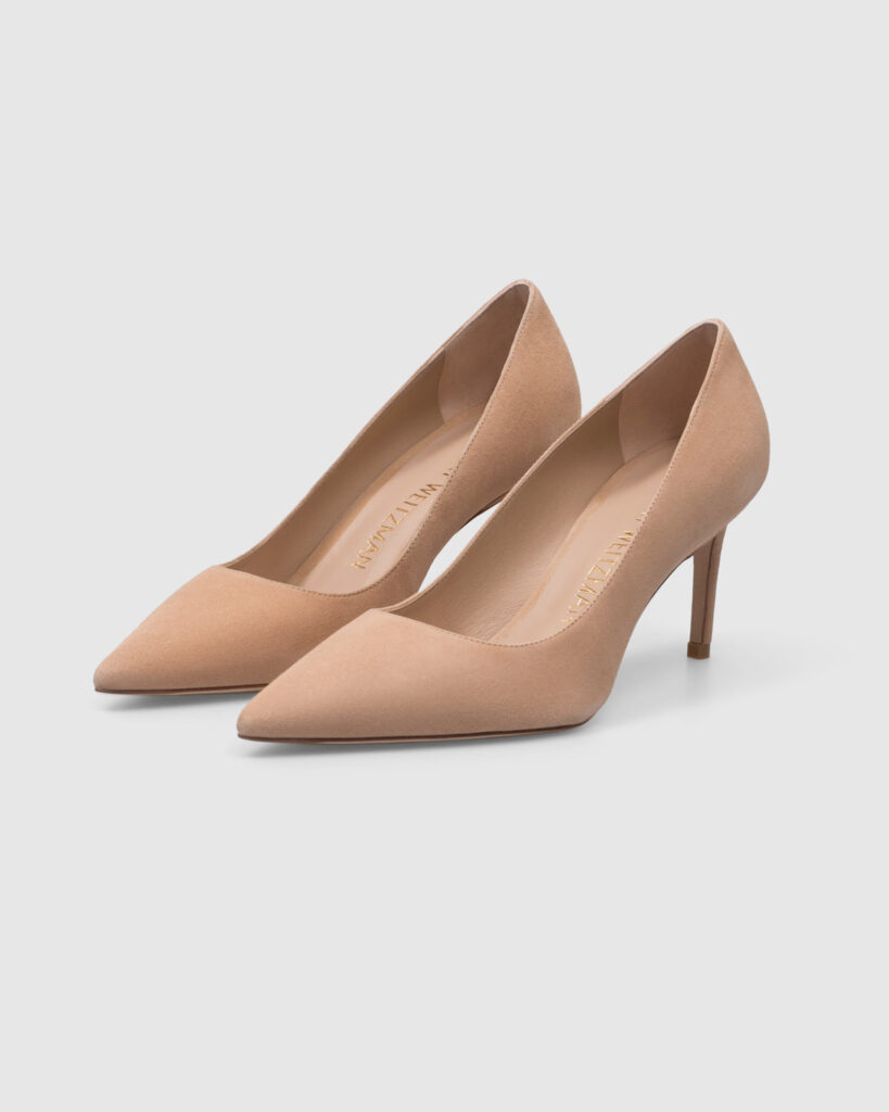 Pair of Stuart Weitzman nude/beige suede pointed-toe high heel pumps with thin heels, photographed for e-commerce on a clean, light grey background.