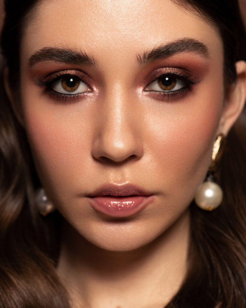 Final retouched high-end beauty portrait of a woman with long wavy brown hair, featuring flawless skin and subtle professional makeup