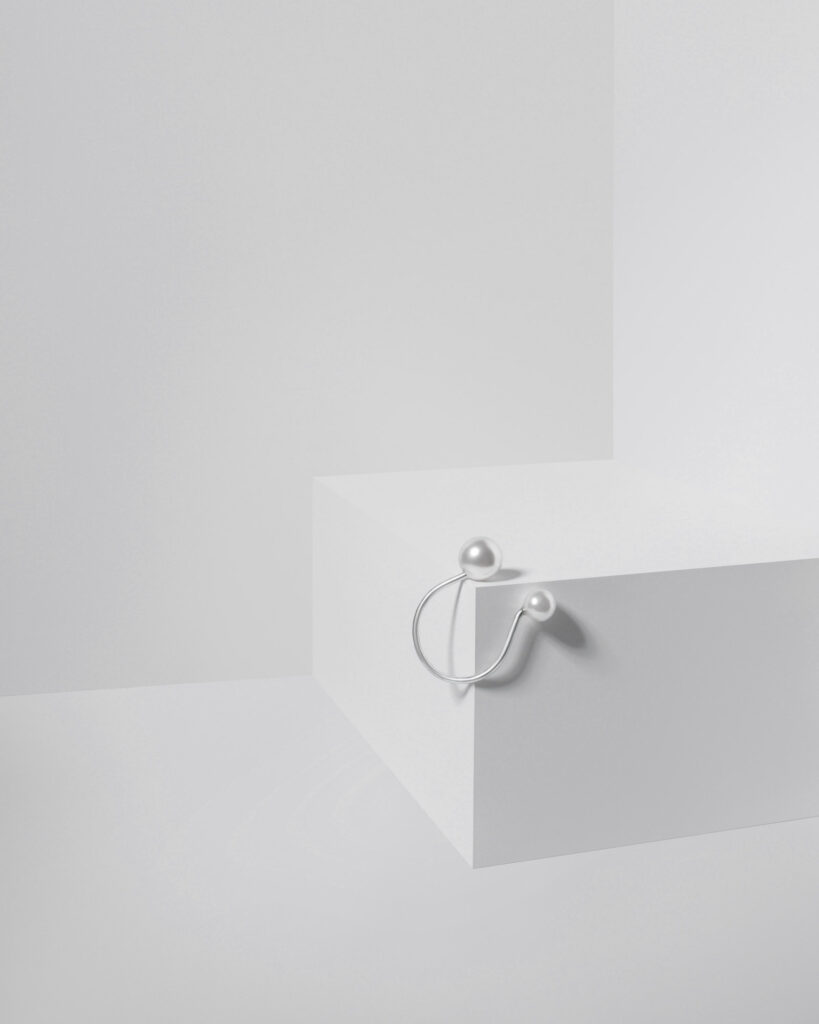 Modern silver ear cuff with two white cultured pearls of different sizes, elegantly positioned on the edge of a white geometric studio prop.